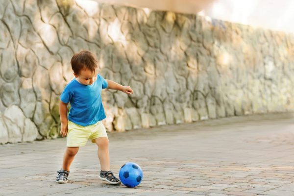 When do babies learn to kick a ball?
