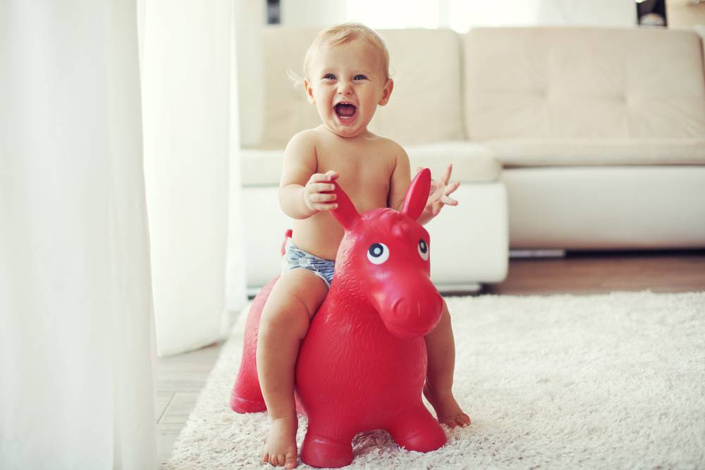 baby laughing while sitting on a toy horse