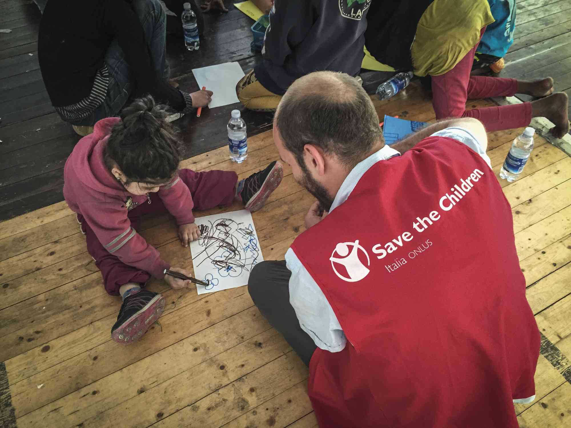 man working for Save the Children watches a girl draw