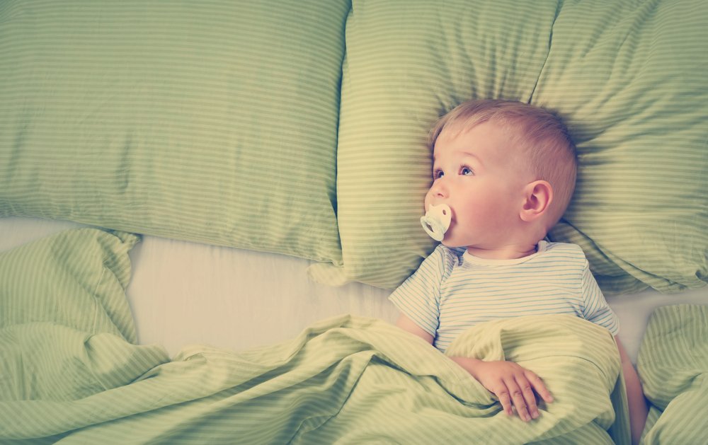baby with pacifier laying in bed