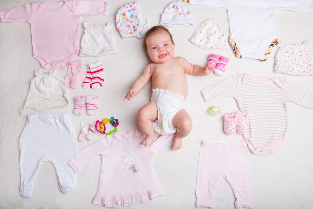 baby girl surrounded by baby clothes