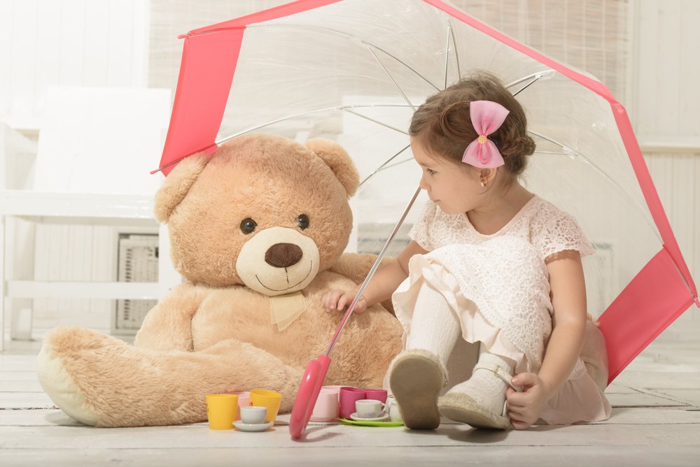 little girl sitting under an umbrella with a teddy bear