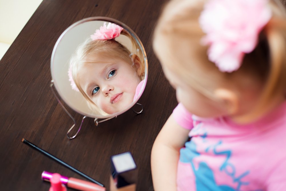 little girl observing her reflection on a mirror