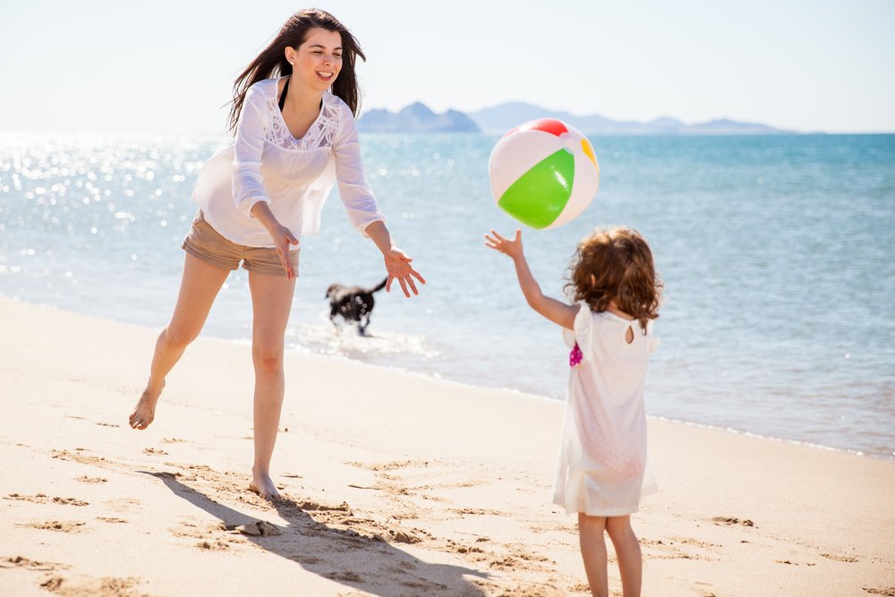 little girl throwing a ball to her mom at the beach