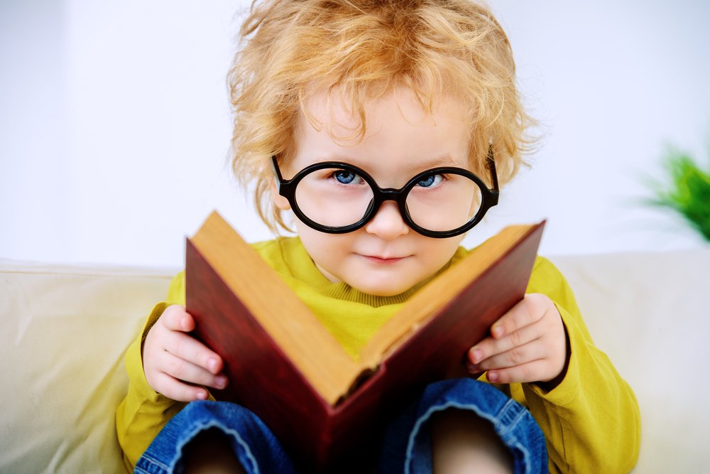 little boy with glasses reading a book for preschoolers