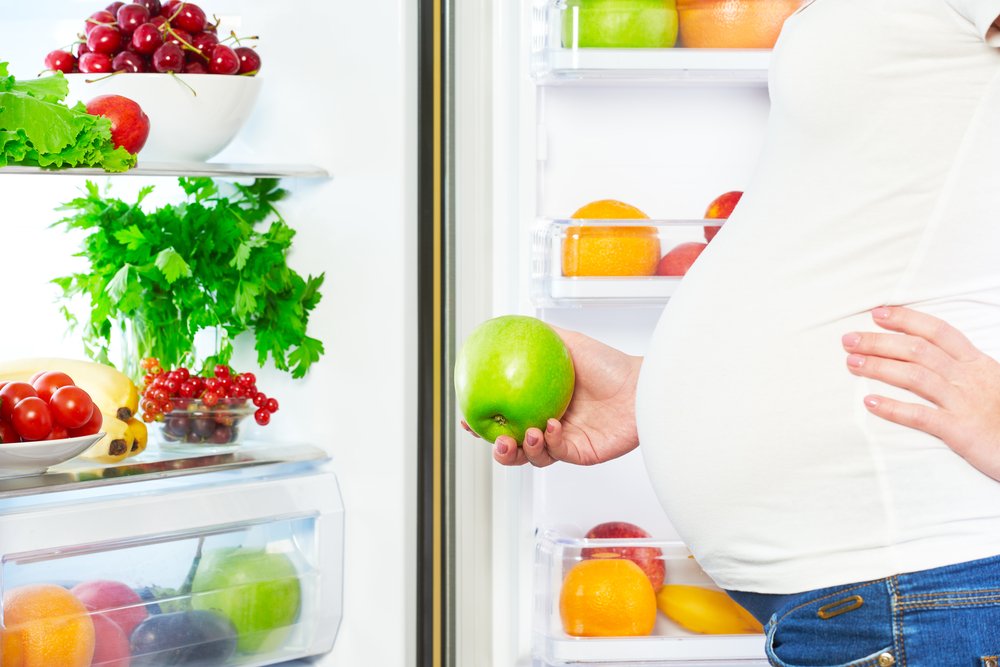 pregnant woman holding a fruit in front of the fridge