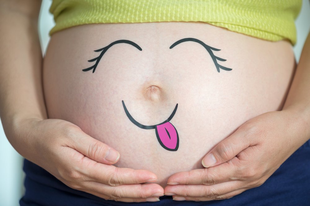 a smiley face drawn on a pregnant woman's belly