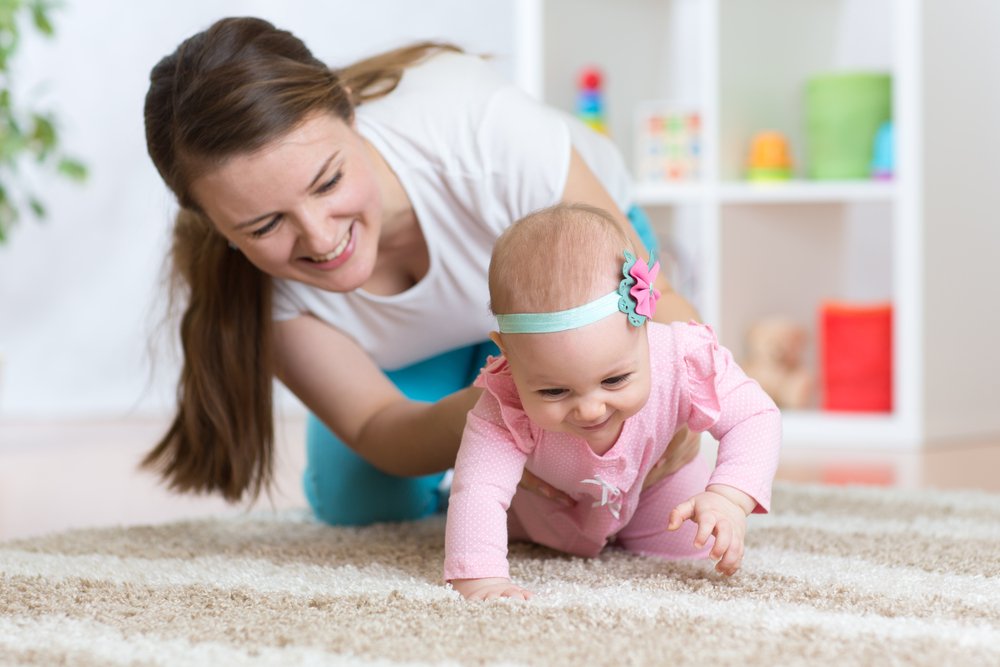 at what age do babies crawl? mom helping her baby crawl
