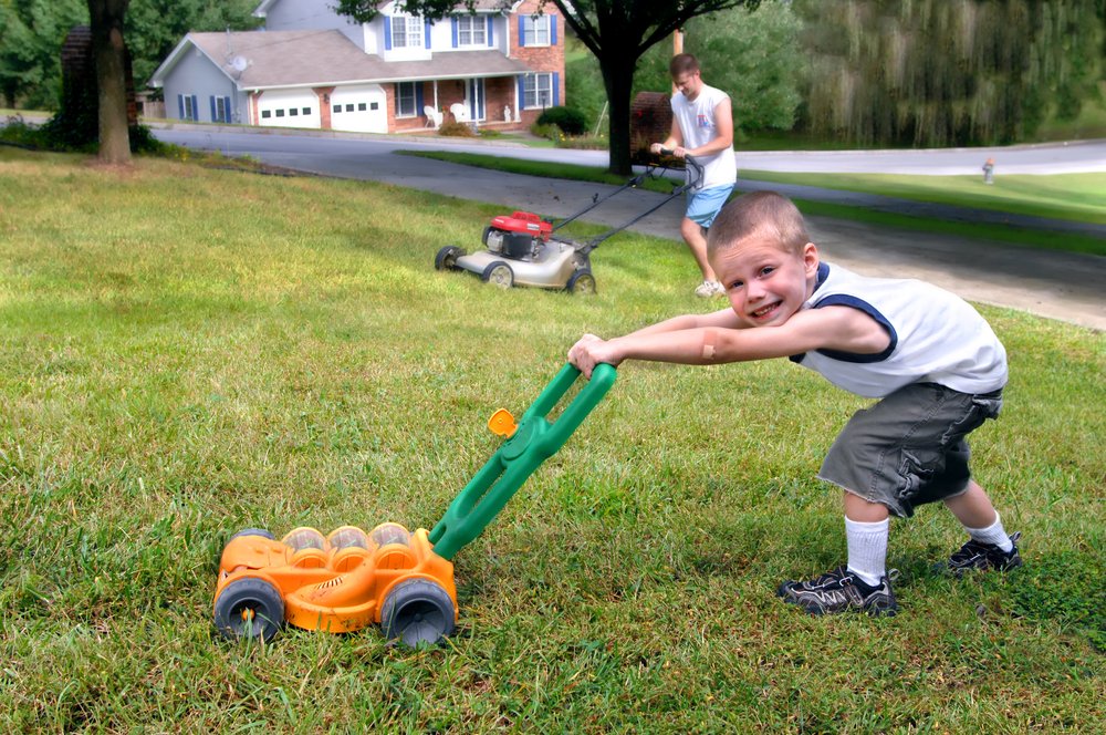 little boy pretending to mow the lawn as his father