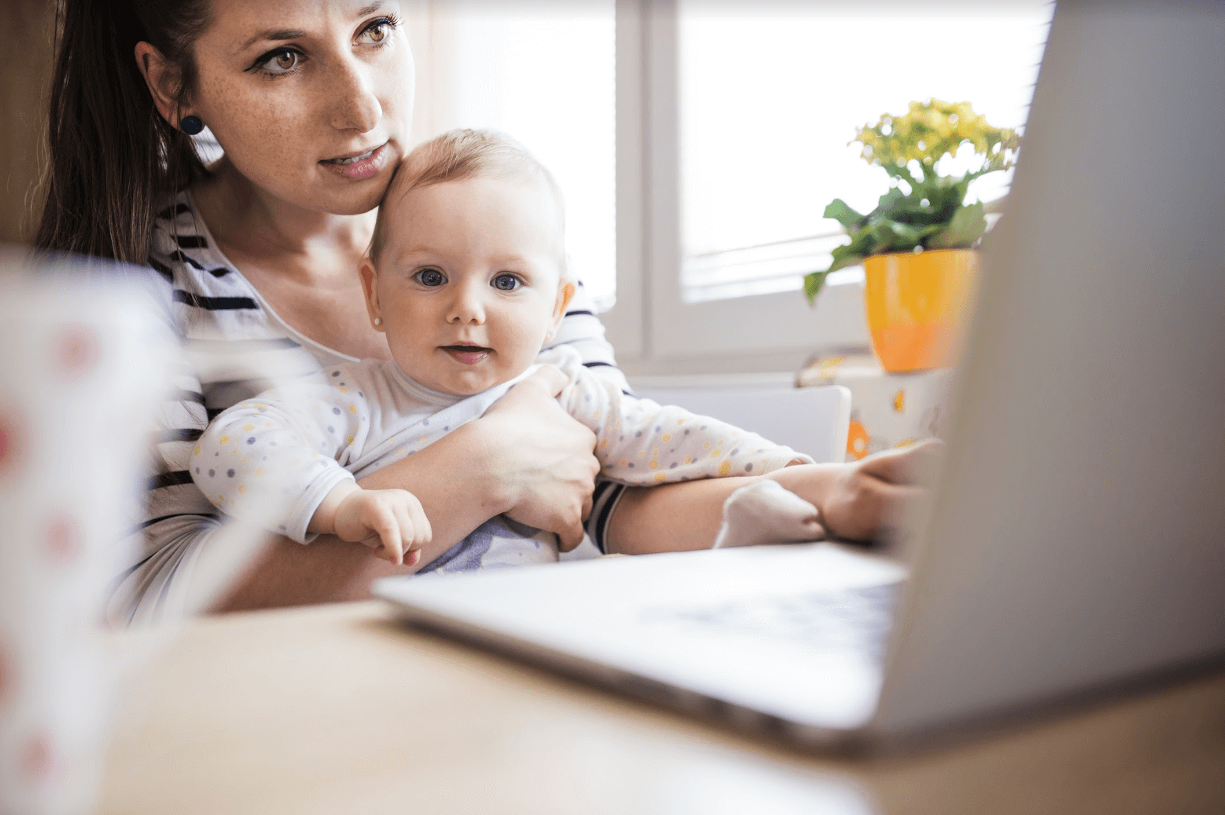 mother checking her laptop while holding her baby