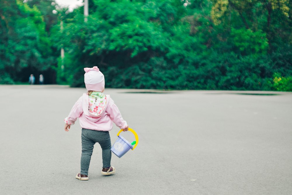 little girl walking while holding a plastic bucket