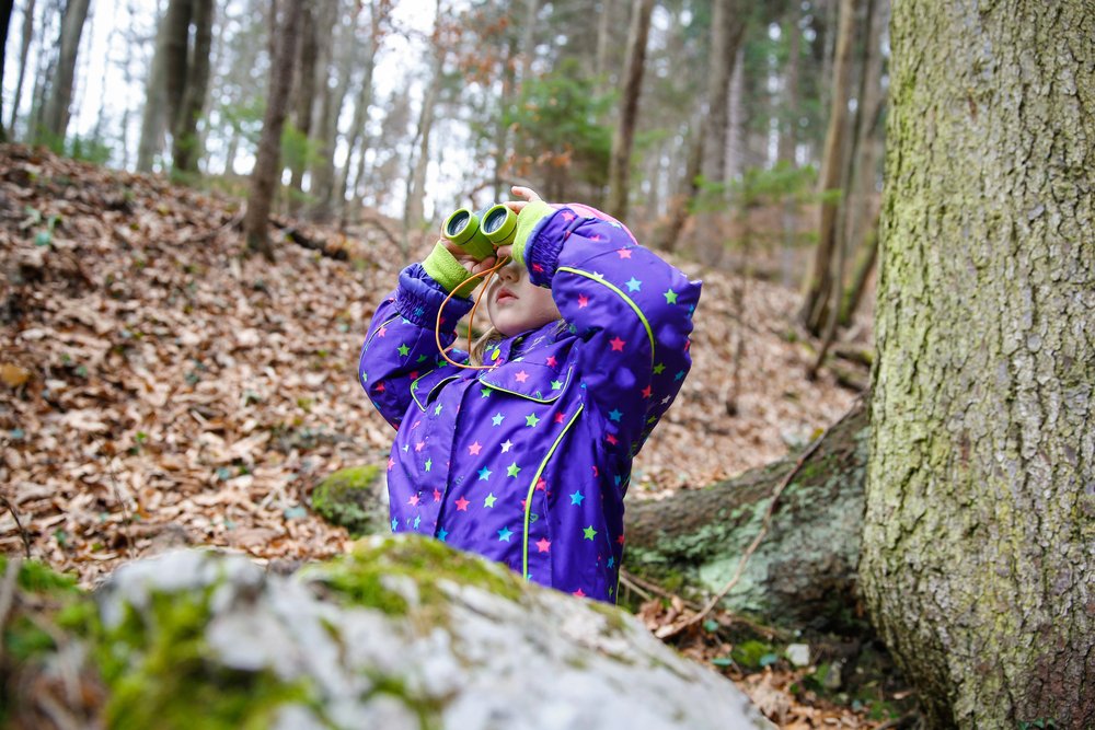 little girl with binoculars in the woods