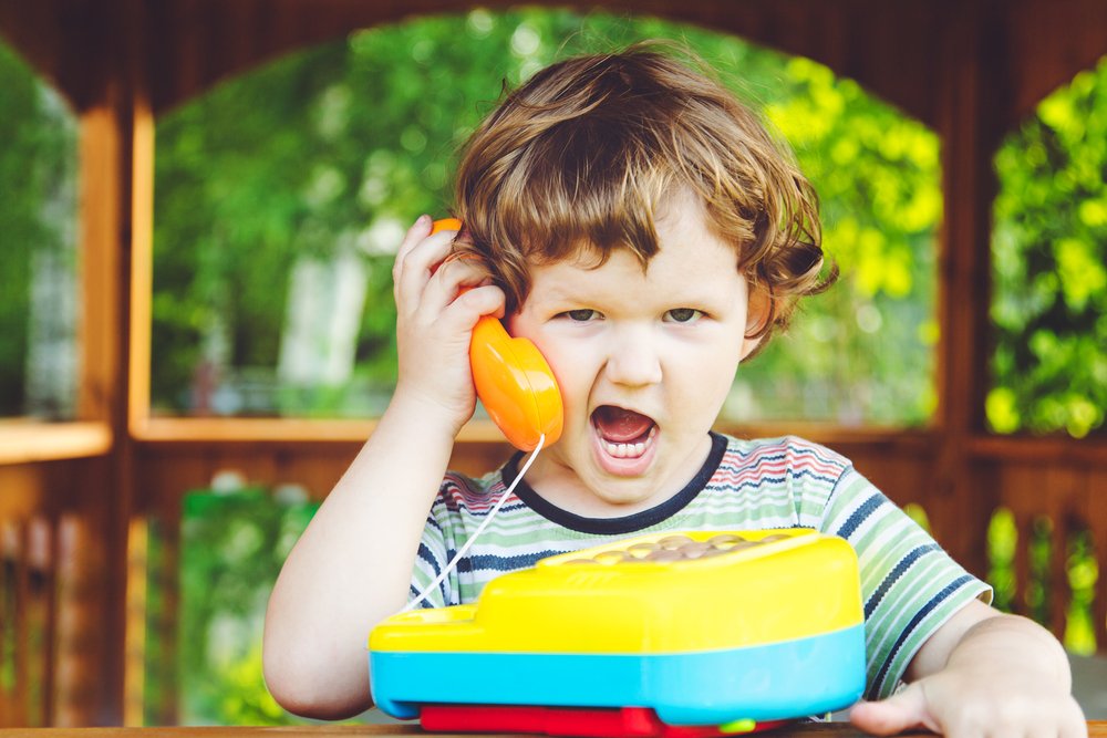 little boy holding a toy telephone and acting confused