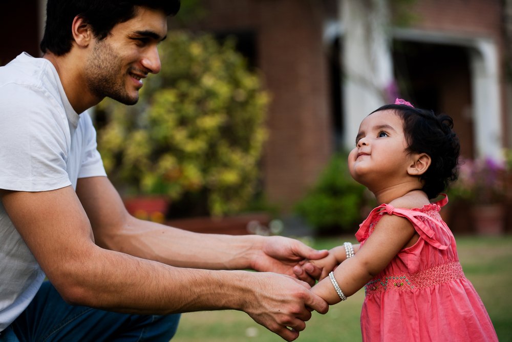 baby girl standing up while holding her father's hands