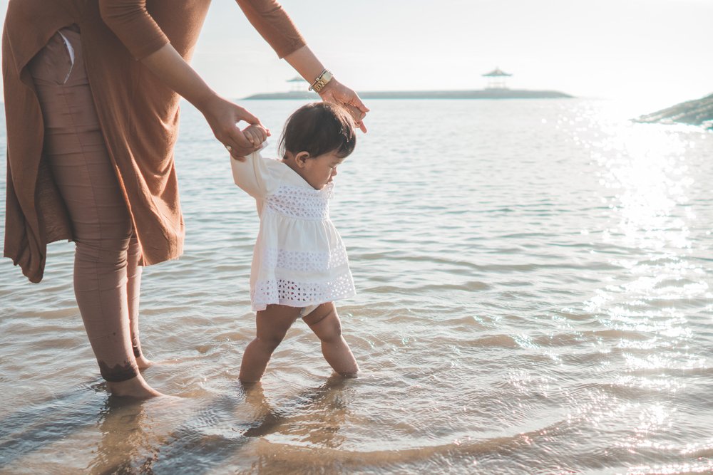 mom holding her baby's hands while walking on the beach