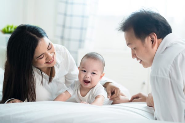 mom and dad helping baby to crawl on the bed